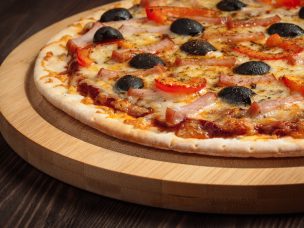 Panoramic image of ham pizza with capsicum and olives on wooden board on table close up