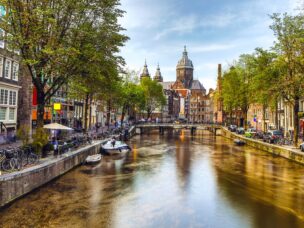 The most famous canals and embankments of Amsterdam city during sunset. General view of the cityscape and traditional Netherlands architecture.