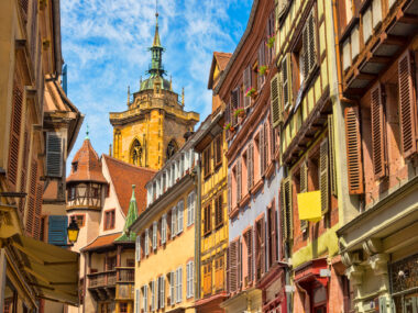 View of residential building with beautiful old half-timbered fronts and colorful shutters and a nice view of the cathedral in the background in the beautiful old French town of Colmar in Alsace.