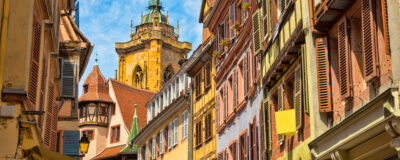 View of residential building with beautiful old half-timbered fronts and colorful shutters and a nice view of the cathedral in the background in the beautiful old French town of Colmar in Alsace.